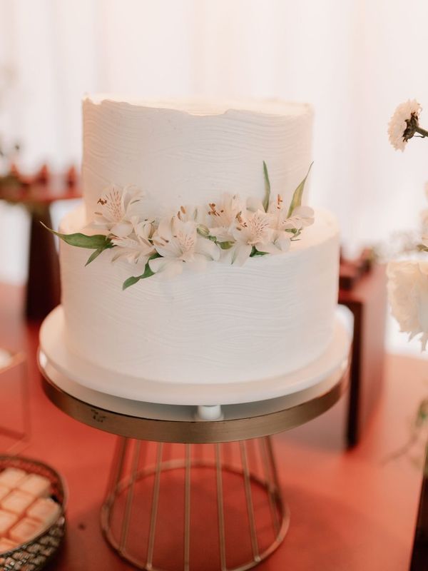 A two-tier white wedding cake decorated with fresh white flowers on a gold stand